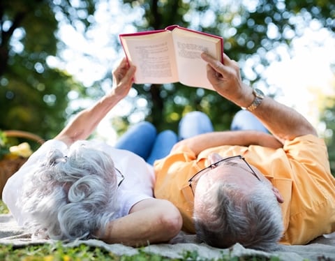 Picture of an older couple laying on the grass reading the same book