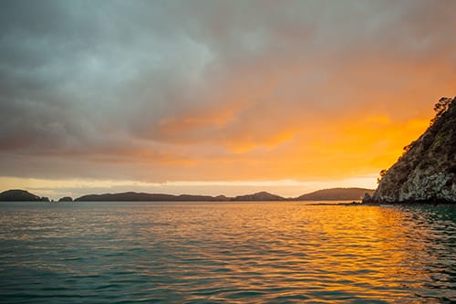 Golden sunset over calm water in the Bay of Islands near the coastline