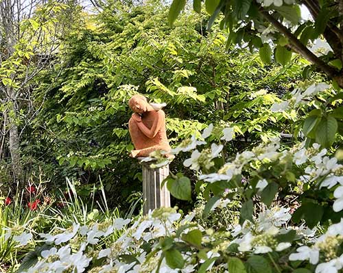 Terracotta sculpture of a seated woman with a white bird on her shoulder, framed by flowering white blossoms and lush spring foliage in the gardens at Treghan Lodge, Kerikeri. Terracotta sculpture of a seated woman with a white bird on her shoulder, framed by flowering white blossoms and lush spring foliage in the gardens at Treghan Lodge, Kerikeri.